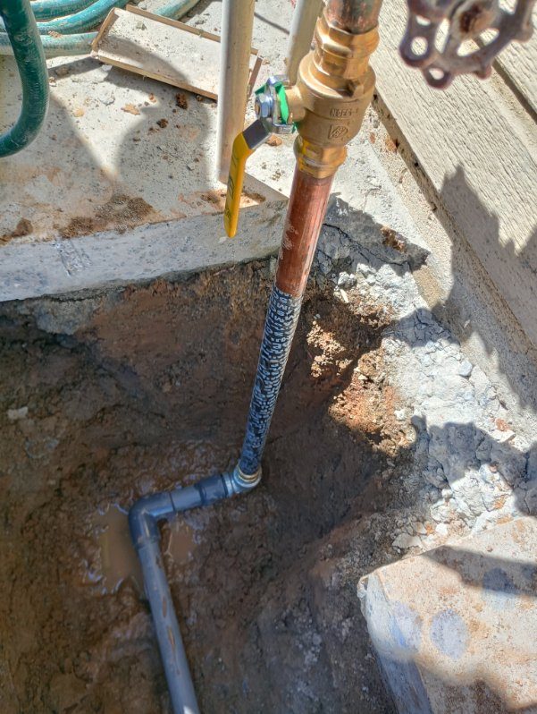Copper and PVC water pipes installed in outdoor trench with soil and concrete surrounding