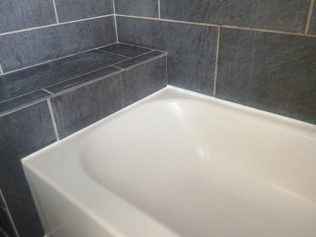 Modern bathroom with white soaking tub and dark gray tile walls with light grout lines