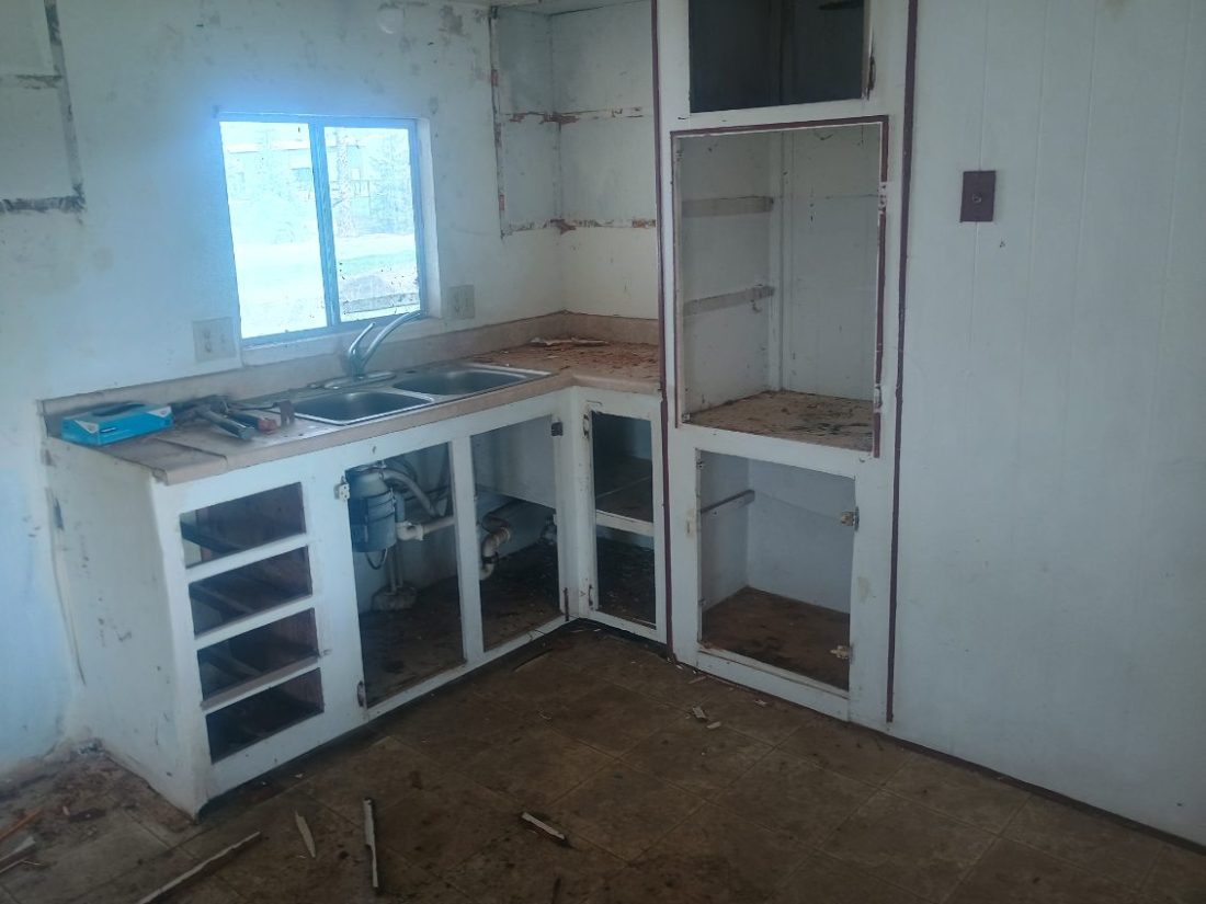 Unfinished kitchen interior with white cabinetry, stainless steel sink, and bare concrete flooring under construction