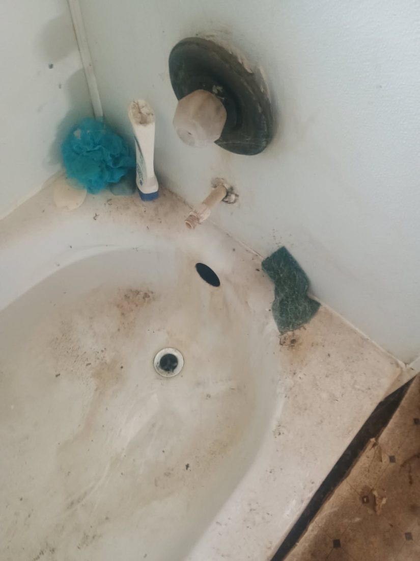 Dirty bathtub with cleaning supplies and stains on walls