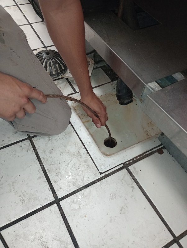 Plumber using drain snake to clear bathroom sink drain through floor opening