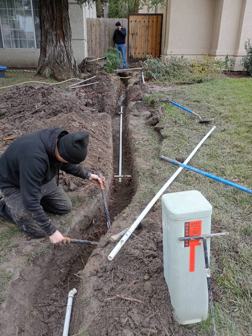 Workers installing underground irrigation or utility pipes in residential yard trench