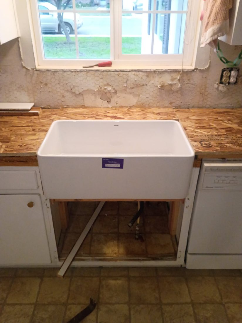 White farmhouse kitchen sink installed in wooden countertop below window