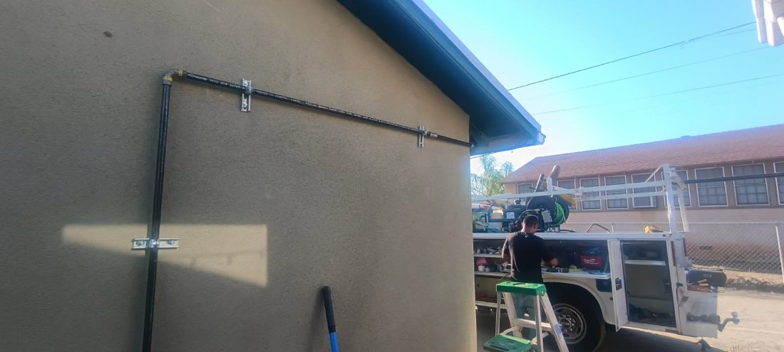 Professional gutter installation on tan residential building with metal brackets and downspout system