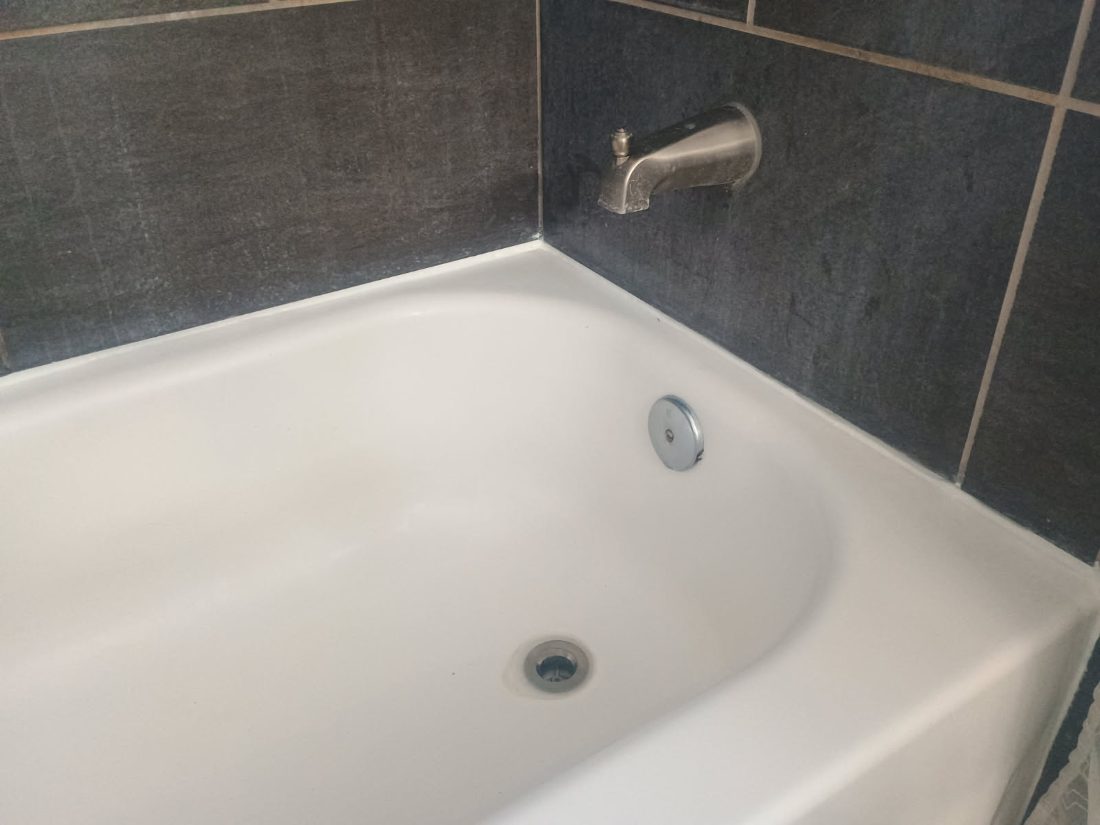 White bathtub with chrome spout and dark gray tile surround in bathroom