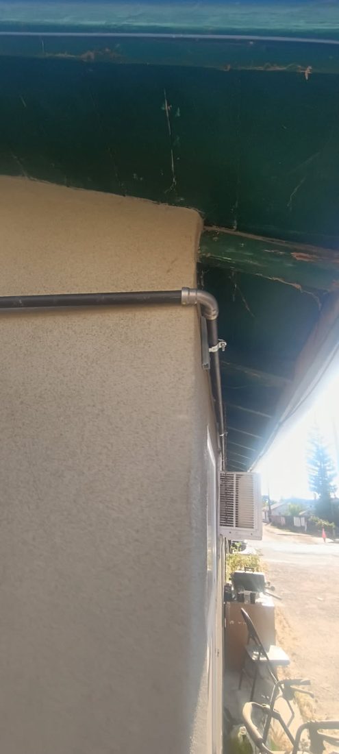 Gutter downspout on beige building exterior with water view in background
