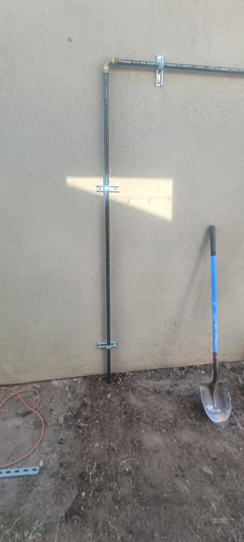 Metal fence frame with horizontal and vertical rails mounted on concrete wall with shovel nearby