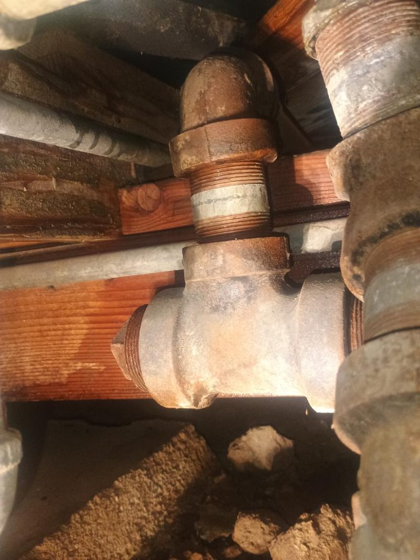 Corroded copper pipe fittings and brass valves with mineral deposits and patina