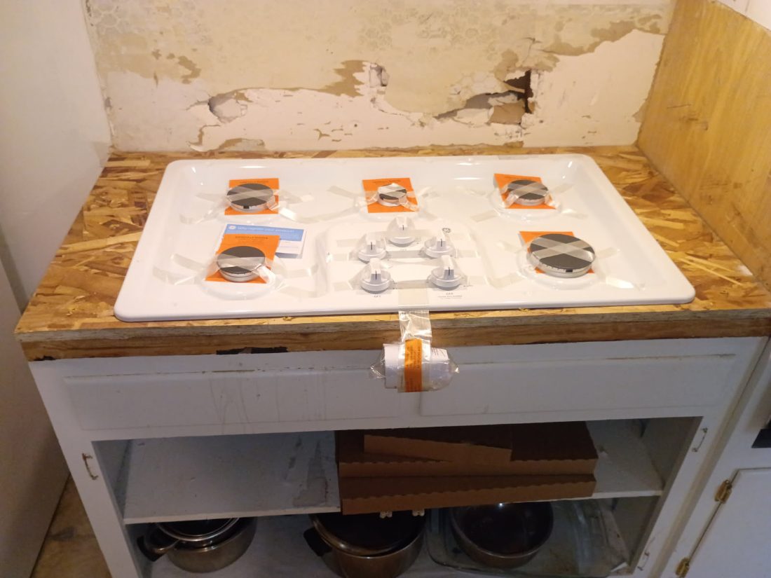Stovetop display with orange packaged burner components and control knobs on white surface