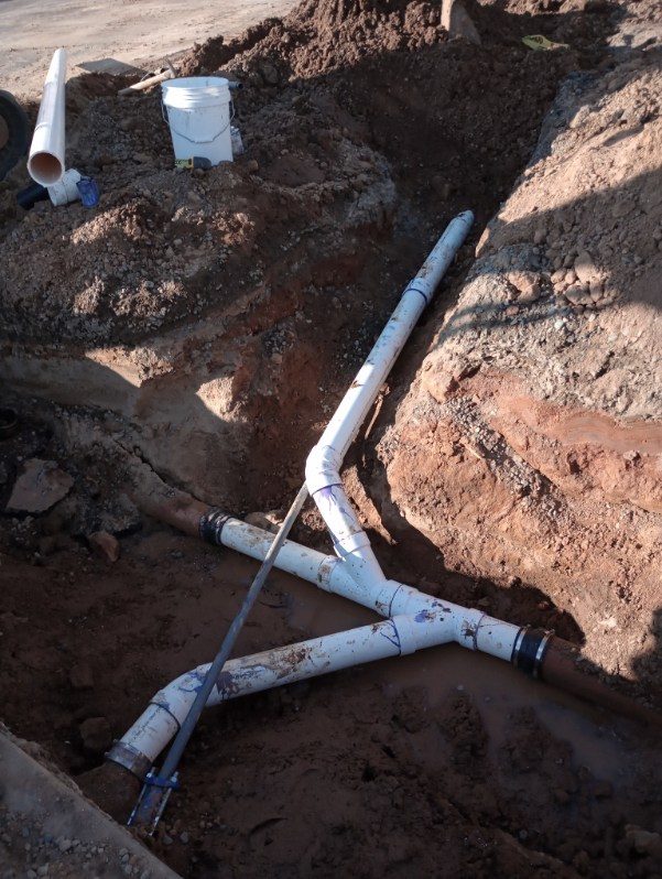 Underground plumbing pipes and white bucket in excavated trench during installation