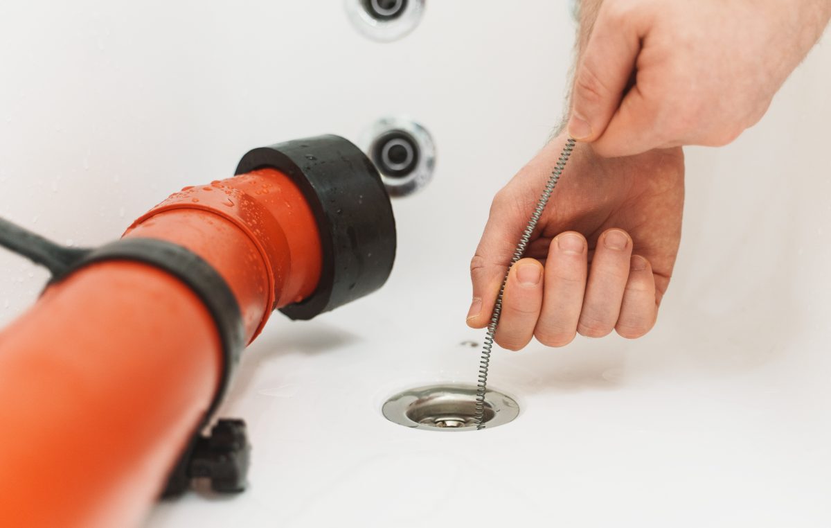 Plumber using motorized drain snake to clear a sink drain opening