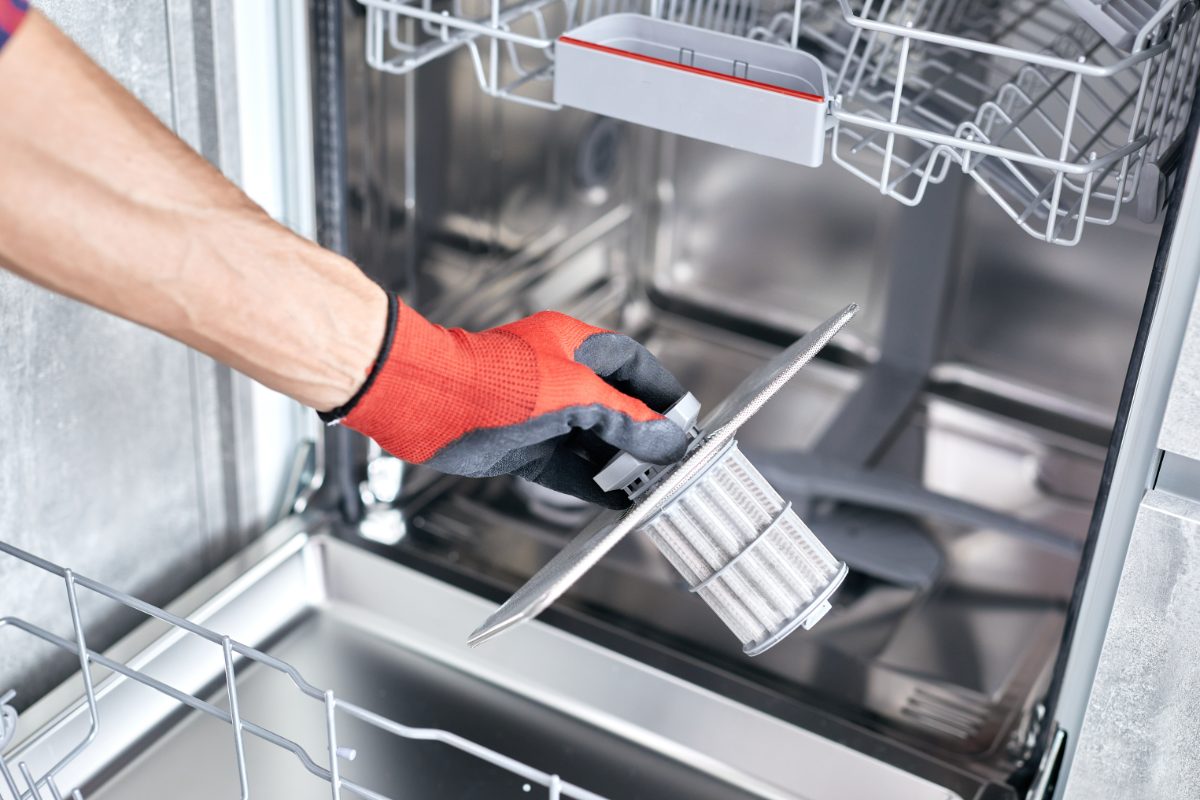 Person in red gloves cleaning dishwasher filter with brush