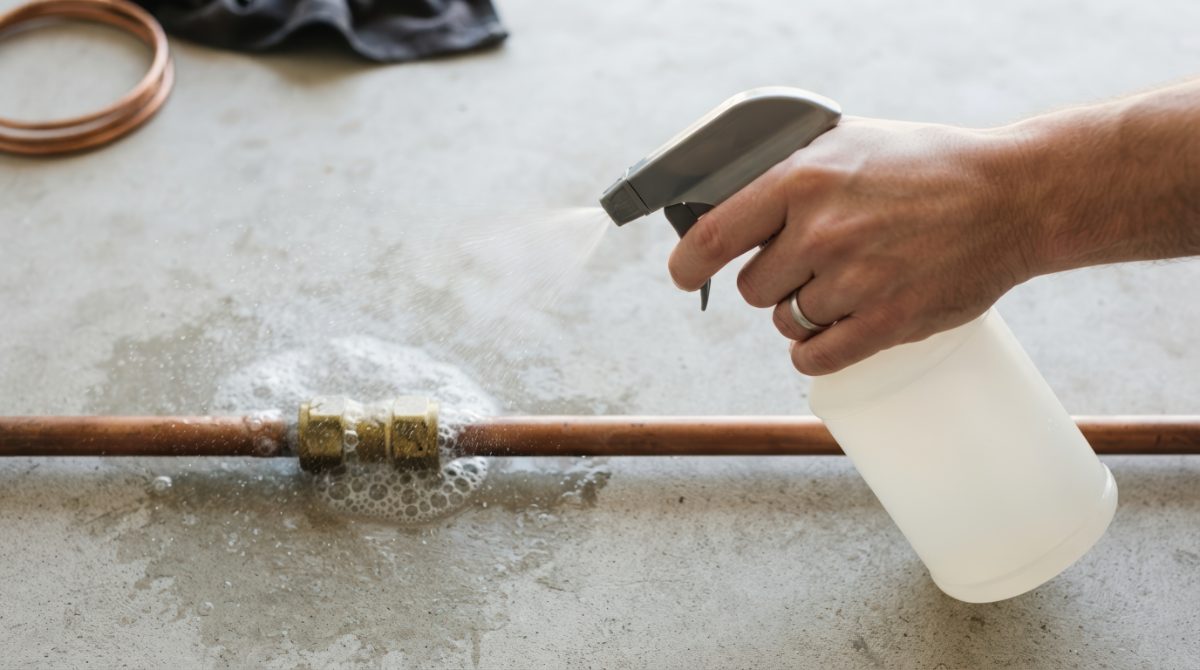 Worker holding spray bottle while cleaning rusty metal pipe